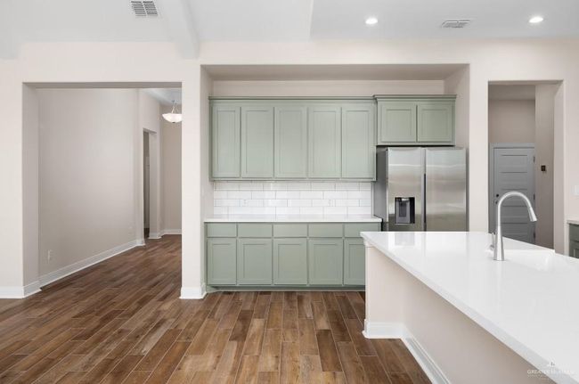 Kitchen featuring dark wood finished floors, green cabinets, visible vents, stainless steel refrigerator with ice dispenser, and a sink | Image 8