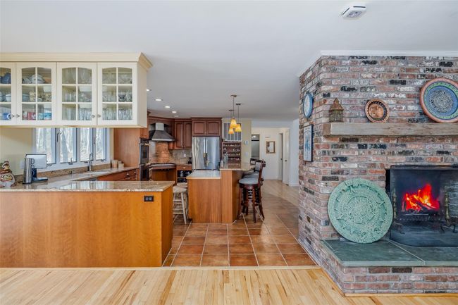 Kitchen featuring glass insert cabinets, a fireplace, freestanding refrigerator, wall chimney exhaust hood, and a sink | Image 15