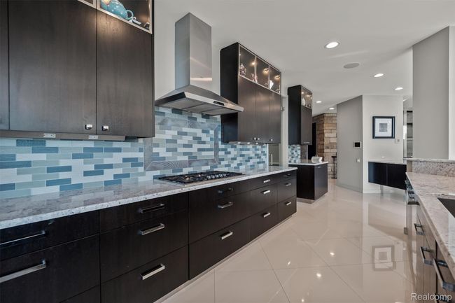 Kitchen with modern cabinets, wall chimney range hood, light tile patterned floors, backsplash, and light stone countertops | Image 14