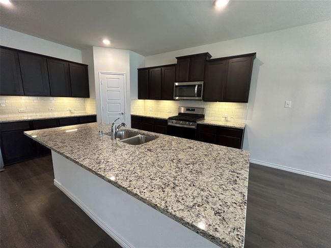 Kitchen featuring stainless steel appliances, a sink, light stone counters, dark wood-type flooring, and a kitchen island with sink | Image 19