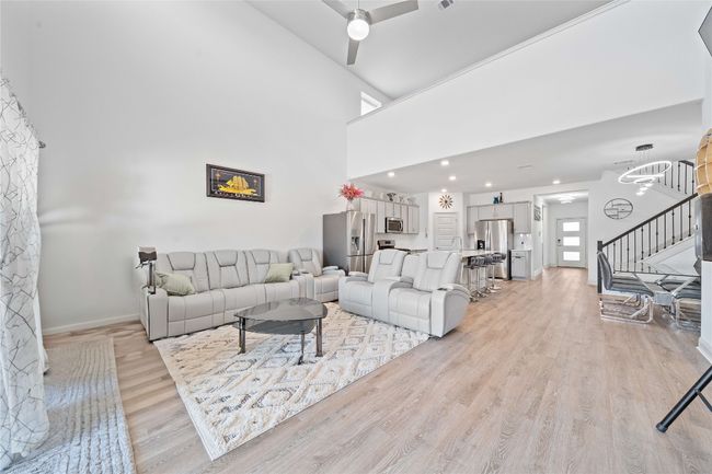 Living area with ceiling fan, light wood-type flooring, a towering ceiling, stairs, and baseboards | Image 16