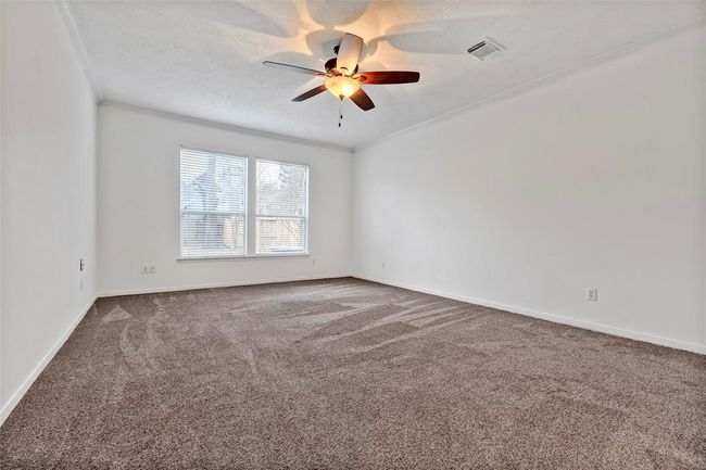 This spacious room features neutral walls, plush carpeting, and ample natural light from two large windows. A ceiling fan adds comfort and style. Perfect for a bedroom or living space. | Image 13