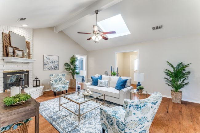 Living room featuring ceiling fan, wood finished floors, a brick fireplace, and a skylight | Image 10