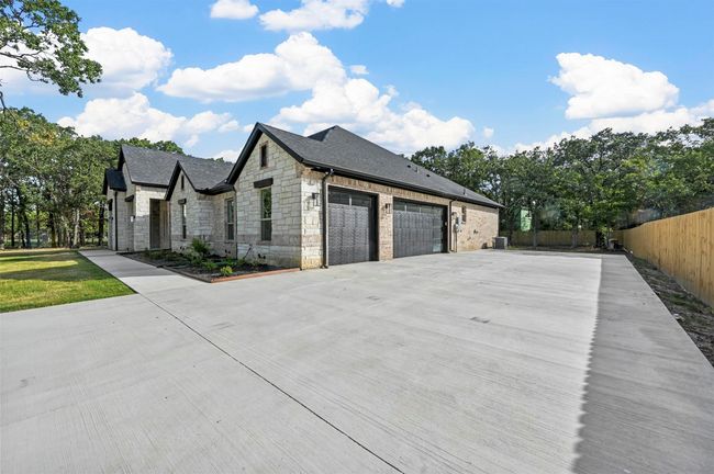 View of side of home with an attached garage, fence, stone siding, concrete driveway, and roof with shingles | Image 8