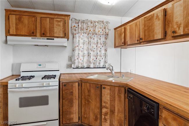 Kitchen with black dishwasher, white gas range oven, brown cabinetry, under cabinet range hood, and a sink | Image 12