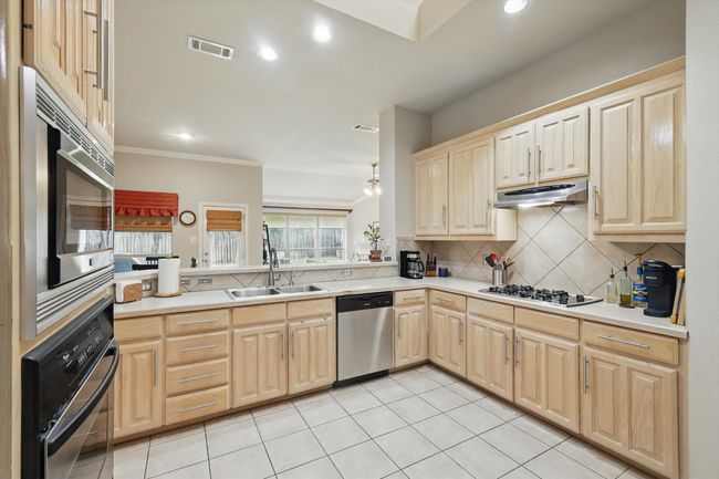 Kitchen featuring visible vents, light brown cabinets, under cabinet range hood, a sink, and appliances with stainless steel finishes | Image 15