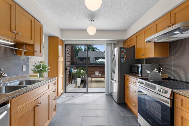 Kitchen featuring stainless steel appliances, under cabinet range hood, tasteful backsplash, a textured ceiling, and dark tile patterned flooring | Image 15
