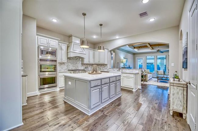 This kitchen features modern design with a spacious island, stainless steel appliances, and pendant lighting. It opens to a cozy living area with large windows for natural light and a view of the backyard. The hardwood floors and neutral tones create a warm, inviting atmosphere. | Image 25