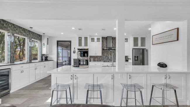 Kitchen featuring appliances with stainless steel finishes, wall chimney exhaust hood, beverage cooler, decorative backsplash, and a kitchen bar | Image 17