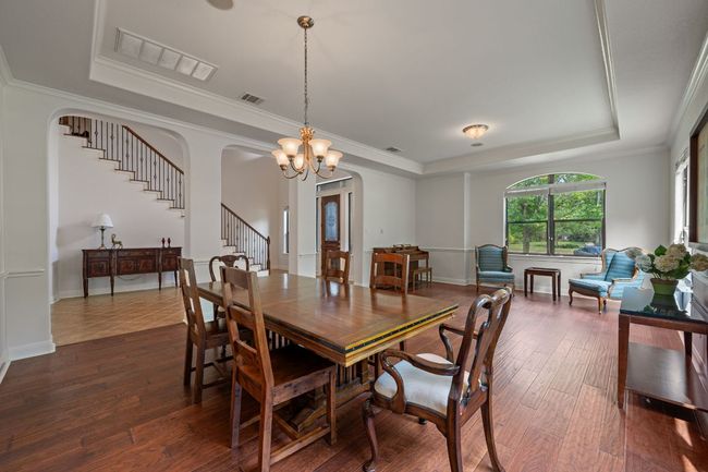 Dining area featuring visible vents, a tray ceiling, dark wood-style flooring, a notable chandelier, and stairs | Image 15