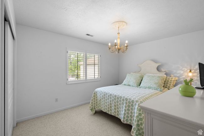 Bedroom featuring light colored carpet, a notable chandelier, a textured ceiling, baseboards, and visible vents | Image 28