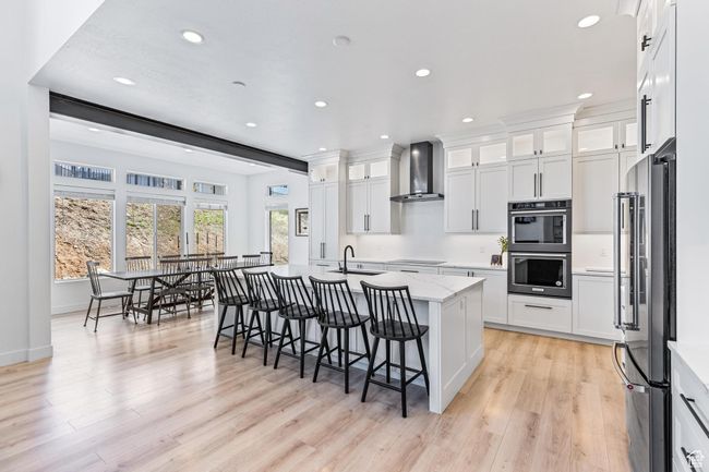 Kitchen featuring wall chimney exhaust hood, black electric cooktop, high end fridge, recessed lighting, and double oven | Image 55