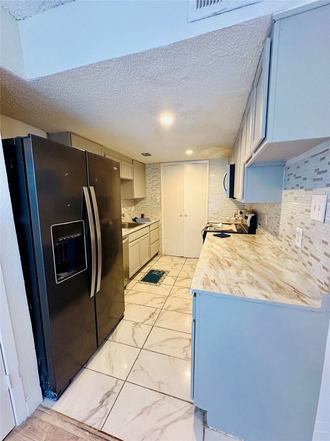 Kitchen featuring black appliances, a textured ceiling, light countertops, decorative backsplash, and light marble finish flooring | Image 4