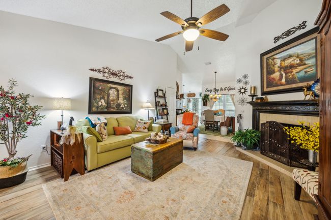 Living area featuring a ceiling fan, hardwood / wood-style floors, high vaulted ceiling, a tile fireplace, and baseboards | Image 8