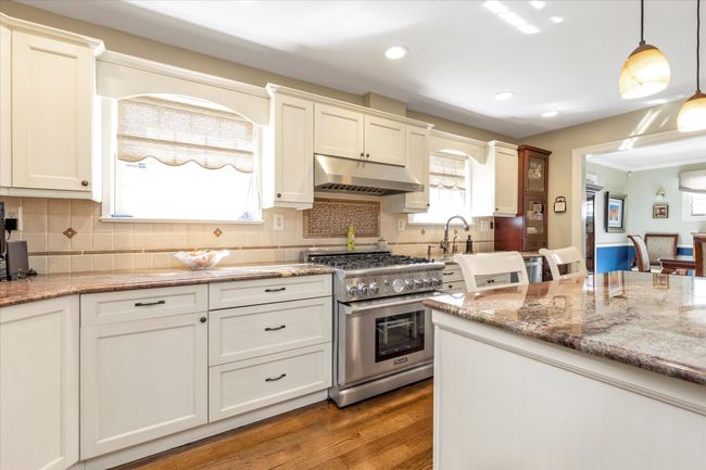 Kitchen with under cabinet range hood, wood finished floors, decorative light fixtures, stainless steel stove, and tasteful backsplash | Image 5