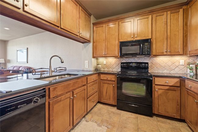 Kitchen featuring tasteful backsplash, brown cabinetry, open floor plan, black appliances, and a sink | Image 11