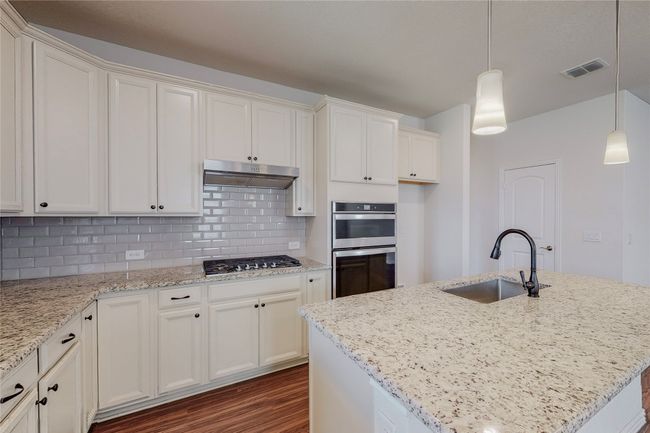 Kitchen featuring a sink, stainless steel appliances, under cabinet range hood, dark wood finished floors, and decorative backsplash | Image 9