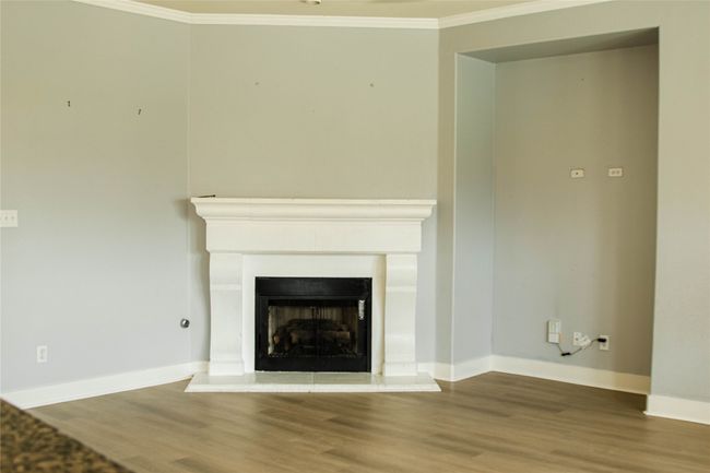 Unfurnished living room with ornamental molding, wood finished floors, and a fireplace with raised hearth | Image 6