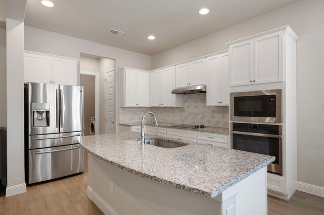 Kitchen with stainless steel appliances, a sink, under cabinet range hood, light wood-style flooring, and white cabinetry | Image 6