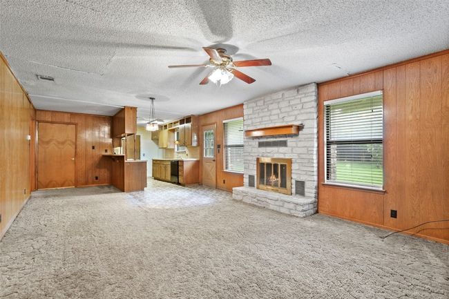 Unfurnished living room featuring wood walls, a ceiling fan, a large fireplace, a textured ceiling, and light colored carpet | Image 15
