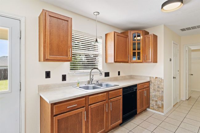 Kitchen with black dishwasher, a sink, light countertops, glass insert cabinets, and pendant lighting | Image 18