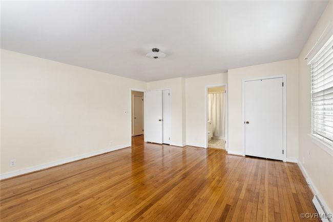 Unfurnished bedroom with connected bathroom, light wood-style flooring, baseboard heating, and baseboards | Image 22