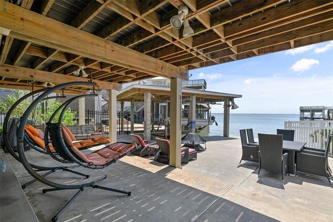 This waterfront property features a spacious outdoor patio with modern hanging chairs, a dining area, and stunning views of the water, perfect for relaxation and entertaining. | Image 5