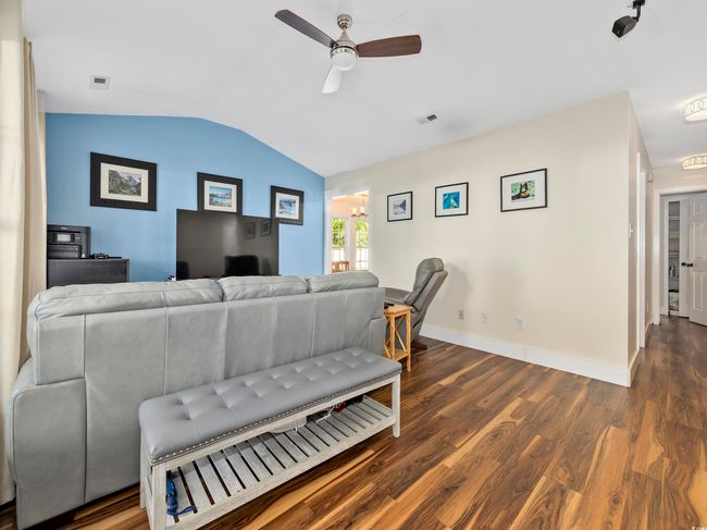 Living area featuring a ceiling fan, visible vents, wood finished floors, baseboards, and lofted ceiling | Image 6