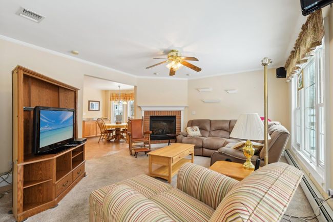 Carpeted living room with ceiling fan, ornamental molding, a brick fireplace, and a baseboard heating unit | Image 13