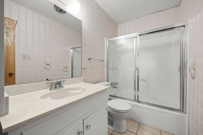 Full bathroom with wallpapered walls, vanity, bath / shower combo with glass door, tile patterned floors, and a textured ceiling | Image 21