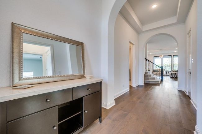 Corridor with stairway, arched walkways, dark wood-style floors, baseboards, and a tray ceiling | Image 4