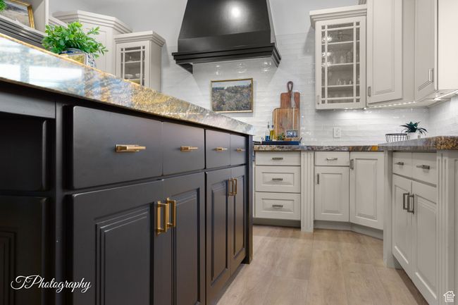 Kitchen featuring glass insert cabinets, white cabinetry, light wood-style flooring, and backsplash | Image 18
