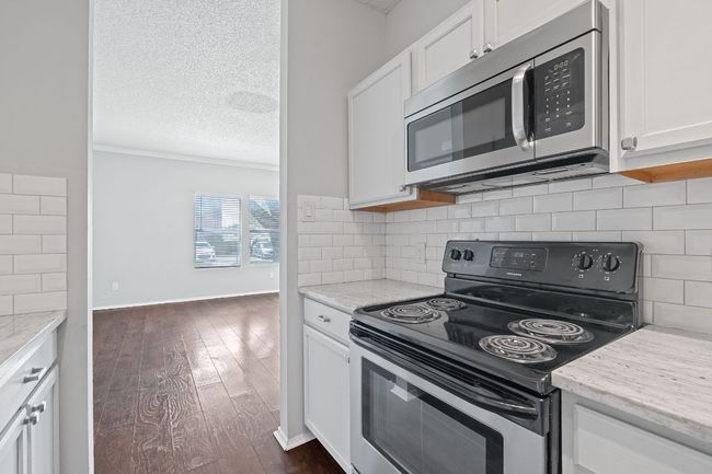 Kitchen featuring dark wood-style flooring, ornamental molding, white cabinetry, tasteful backsplash, and appliances with stainless steel finishes | Image 9