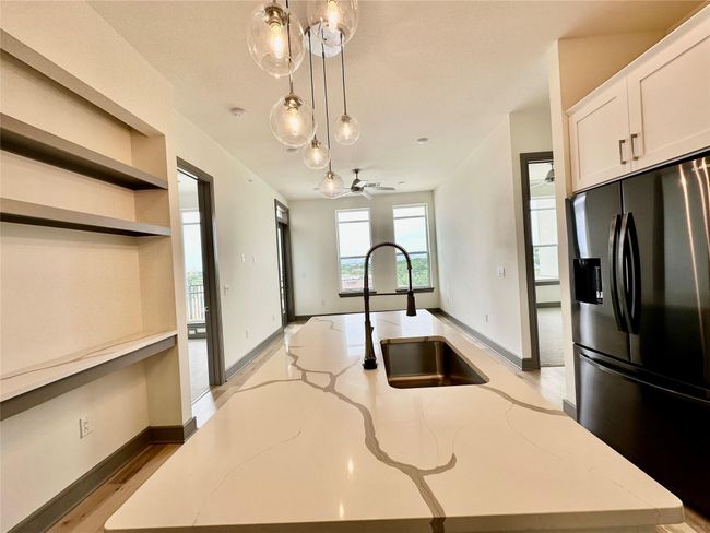 Kitchen featuring a center island with sink, light stone counters, hanging light fixtures, and stainless steel refrigerator with ice dispenser | Image 16