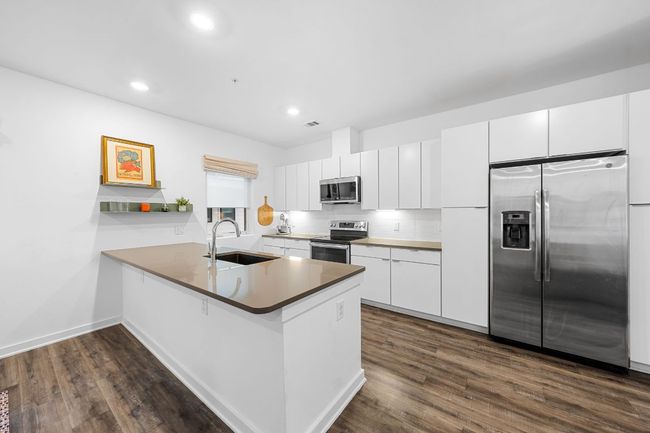 Kitchen featuring dark wood-type flooring, a sink, a peninsula, and appliances with stainless steel finishes | Image 12