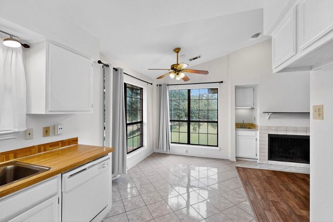 Kitchen featuring dishwasher, a ceiling fan, white cabinetry, lofted ceiling, and a fireplace | Image 4