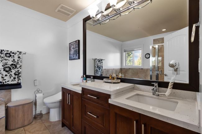 Bathroom with a shower stall, tile patterned floors, toilet, double vanity, and a chandelier | Image 18