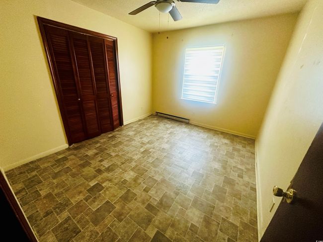 Unfurnished bedroom with baseboard heating, stone finish floors, a closet, baseboards, and ceiling fan | Image 15