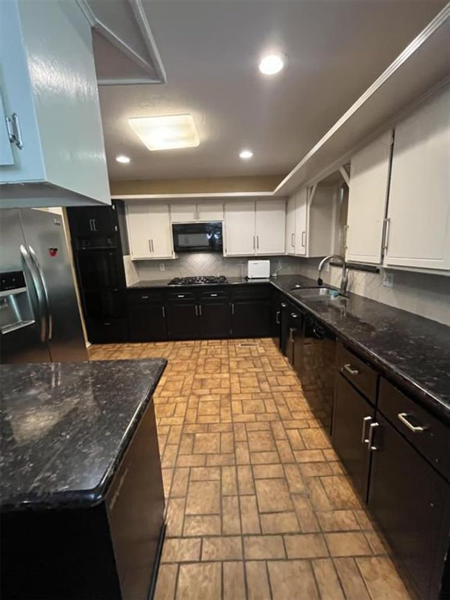 Kitchen with black appliances, white cabinetry, brick patterned floors, recessed lighting, and dark stone counters | Image 28