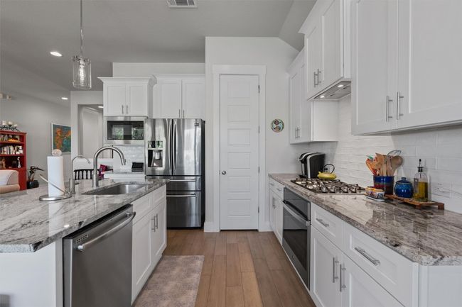 Kitchen with stainless steel appliances, a sink, wood finished floors, white cabinetry, and decorative backsplash | Image 6