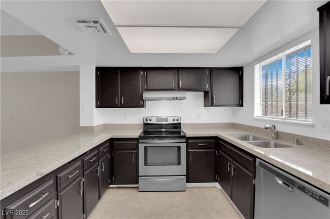 Kitchen featuring stainless steel appliances, a sink, under cabinet range hood, light tile patterned flooring, and light countertops | Image 8