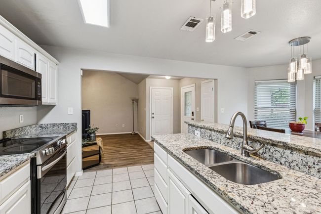 Kitchen featuring stainless steel appliances, light tile patterned floors, white cabinetry, pendant lighting, and light stone counters | Image 5