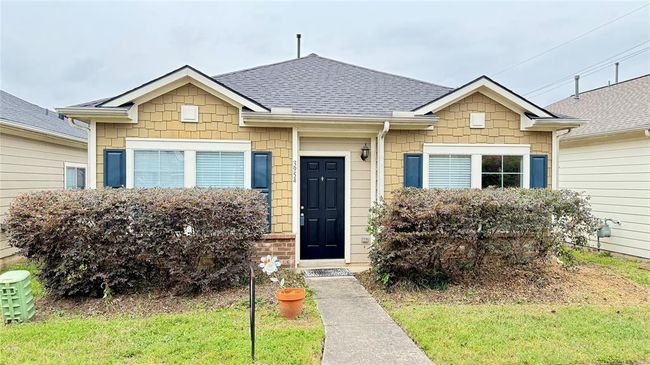 Charming single-story home with a modern exterior. Features a gable roof, beige siding, and blue shutters. A well-maintained front yard with shrubs and a paved walkway leading to a welcoming black front door. Perfect for cozy living. | Image 4