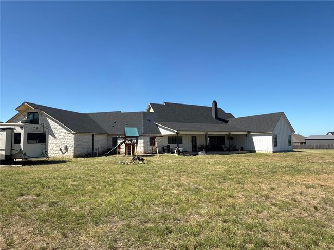 Rear view of property with board and batten siding, a yard, a playground, stone siding, and roof with shingles | Image 34
