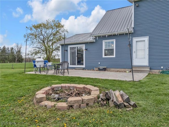 Back of house featuring a lawn, an outdoor fire pit, a patio area, and metal roof | Image 35