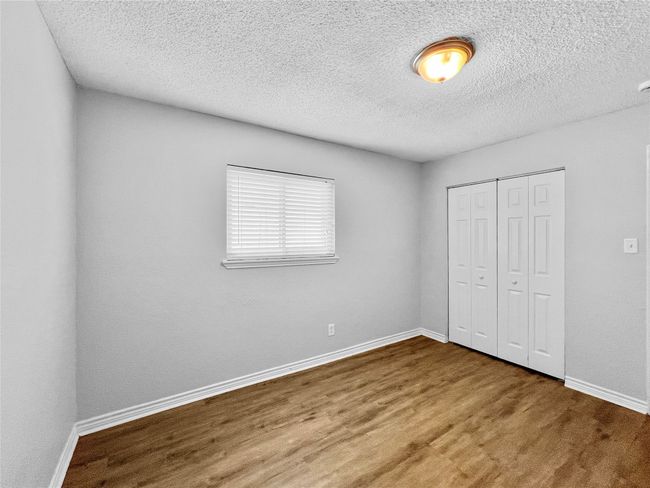 Unfurnished bedroom with a textured ceiling, wood finished floors, and a closet | Image 13