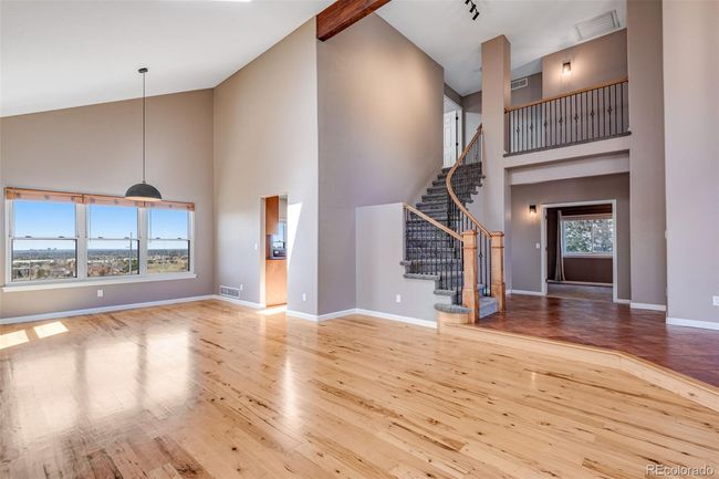 Unfurnished living room featuring baseboards, stairway, visible vents, high vaulted ceiling, and wood finished floors | Image 6