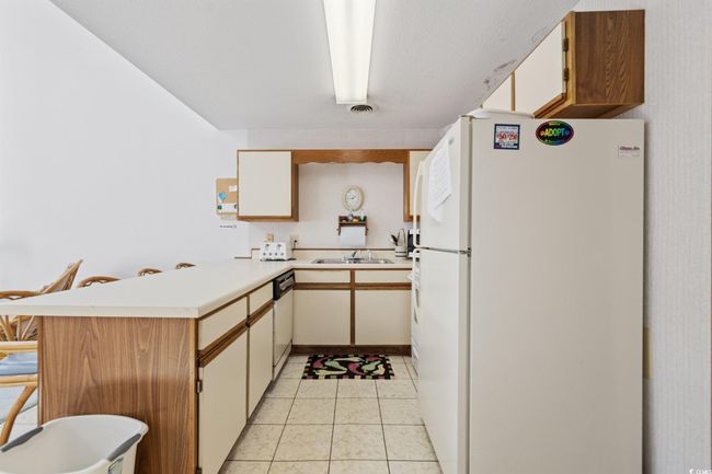 Kitchen featuring white appliances, a peninsula, a sink, light countertops, and light tile patterned flooring | Image 6