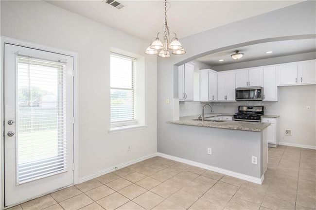 Kitchen featuring stainless steel appliances, white cabinets, a chandelier, light tile patterned floors, and tasteful backsplash | Image 11