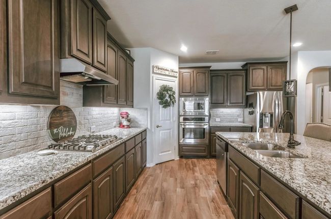 Kitchen featuring arched walkways, light wood-style flooring, under cabinet range hood, stainless steel appliances, and a sink | Image 22